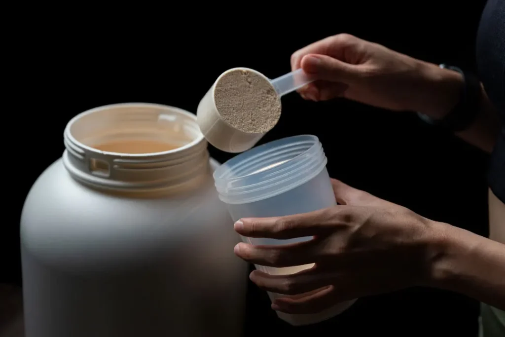 close up of person putting protein powder in container
