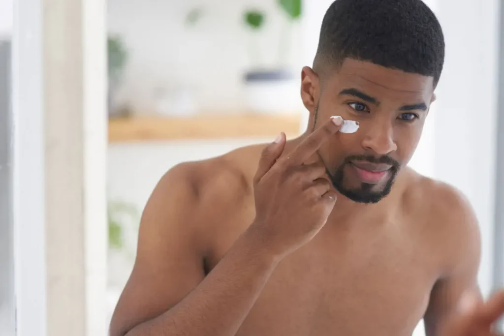 A black man applying cream on his face. 