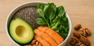 Bowl of high fiber keto foods with avocado, salmon, leafy greens, chia seeds, and mixed nuts on a wooden table in natural light